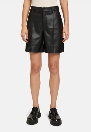 Zwarte leren shorts met een op maat gemaakt ontwerp, voorzien van een vlakke voorkant, riemlussen en subtiele stikdetails. Model gecombineerd met zwarte schoenen.
