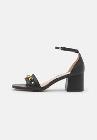 Sandal con tacco alto in pelle nera con cinturino alla caviglia, caratterizzato da un dettaglio in tonalità oro sul cinturino e un tacco a blocco quadrato. Texture liscia.