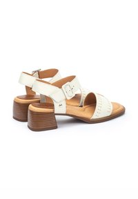Sandalias de cuero blanco con tacón cuadrado, que cuentan con correas ajustables y detalles de costura en la parte superior. Plantilla acolchada marrón.