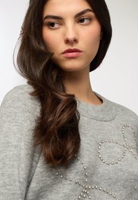 Pullover grigio realizzato in materiale morbido, con un motivo decorativo di perline incorporate. Collo e polsini a costine per un tocco di texture in più.