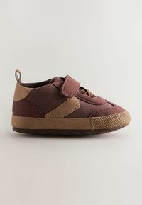 Sneaker marron en tissu texturé avec une sangle velcro. Présente des accents beiges et une semelle en caoutchouc avec un texture à motifs.