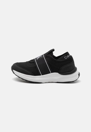 Schwarzer Slip-On-Sneaker mit weißer Sohle und elastischem Riemen auf der Oberseite, Calvin Klein Markenlogo auf dem Riemen und an der Ferse.
