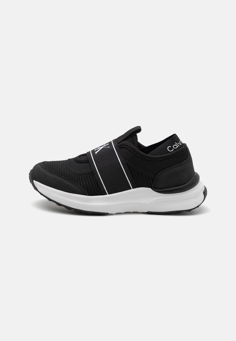 Baskets slip-on noires avec semelle blanche et bande élastique sur le dessus, marquage Calvin Klein sur la bande et le talon.