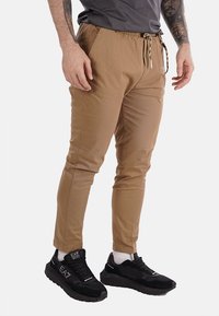 Pantalones jogger de color beige, fabricados en material ligero, con cintura elástica, cierre de cordón y piernas ajustadas. Combinados con zapatillas negras.