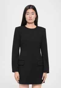 Musta tiukka mekko pitkillä hihoilla, pyöreällä kaula-aukolla ja kahdella ulkopuolisella rintataskulla. Silkkinen kangas rakenteellisilla hartioilla.