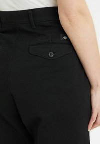 Pantaloni in denim neri con vita aderente, cuciture sottili, due tasche posteriori e un'etichetta sulla vita anteriore.