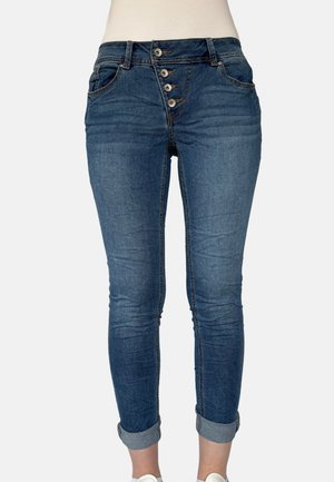 Blaue Denim-Jeans mit hoher Taille, vier sichtbaren Knöpfen, Vordertaschen, hochgekrempelten Säumen, getragen von einer Person mit weißen Sneakers.