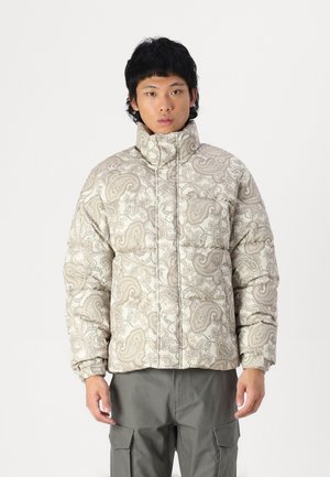 Pehmeä puffer-takki vaaleassa beigevässä, jossa on paisley-kuvio, korkea kaulus ja joustavat hihansuut, yhdistettyinä oliivinvihreisiin cargo-housuihin.