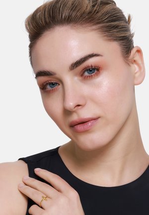 Eine Nahaufnahme einer Person mit blauen Augen und heller Haut, die ein schwarzes Oberteil und einen goldenen Kreuzring trägt. Die Person zeigt eine glatte Haut und ein natürliches Make-up.