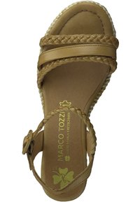 Braune Leder-Sandale mit geflochtenen Riemen und Schnallenverschluss. Die weiche Fußbettung zeigt das bedruckte Markenlogo und ein Kleeblatt-Motiv. Flache Sohle.