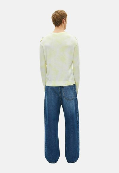 Hellgrüner Tie-Dye-Pullover mit langen Ärmeln und rundem Halsausschnitt, kombiniert mit lockeren blauen Jeans mit einer Gesäßtasche.