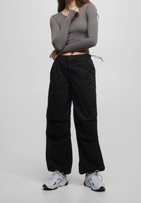 Pantaloni cargo neri con vestibilità ampia e diverse tasche, abbinati a un top grigio a maniche lunghe e corto, completati da scarpe da ginnastica bianche.
