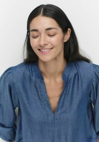 Jeansblus med V-ringning, långa puffärmar och en avslappnad passform. Tyget är ljust blått med en mjuk textur.