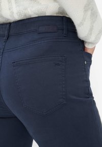 Mørkeblå jeans i bomuldsblanding med en baglomme, der har diskrete syninger og et lille logomærke over linningen.