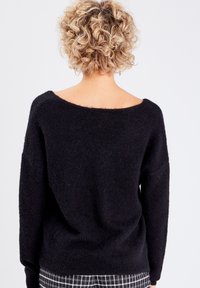 Sort strikket sweater med en bred off-shoulder halsudskæring og lange ærmer. Blød tekstur, afslappet pasform, detaljeret med en ribbede kant.