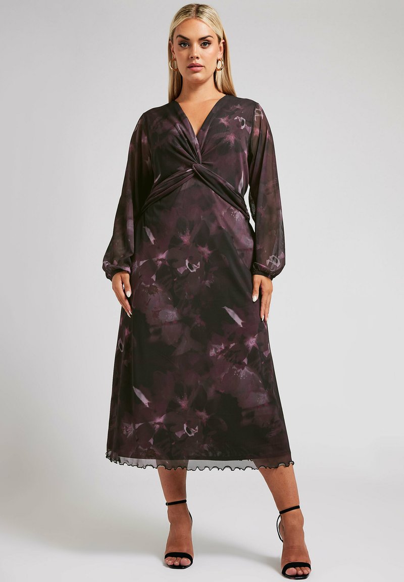 Sukienka w ciemny kwiatowy wzór z głębokim dekoltem w kształcie litery V, skręconym przodem, długimi przezroczystymi rękawami oraz falbaniastym dołem. Materiał jest lekki i zwiewny.