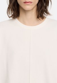 Jasno beżowy sweatshirt z okrągłym dekoltem, z centralnym szwem i gładką, miękką teksturą.