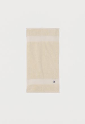 Serviette rectangulaire couleur crème avec un milieu texturé, des bords lisses, et un petit logo sombre représentant un cheval et un cavalier proche d'un coin.