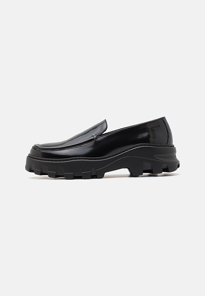Bottines noires en cuir verni à enfiler, avec une semelle en caoutchouc noir épaisse et texturée, et un détail de couture le long du bord.