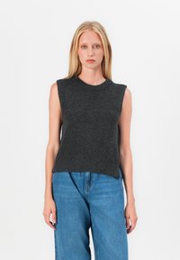 Pull en tricot sans manches gris foncé avec un col rond et une texture côtelée, associé à un pantalon en denim. Design simple et moderne.