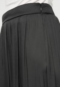 Black pleated skirt featuring a smooth waistband and a discreet zipper at the back, crafted from lightweight, textured fabric.