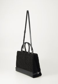 Black bag with a textured, fuzzy surface and smooth leather bottom. Features two top handles and a long adjustable strap.