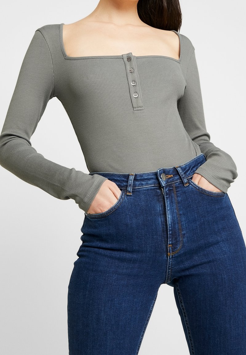 Långärmad, ribbad bodysuit i olivgrått med fyrkantig halsringning och femknäpps stängning, i kombination med högmidjade blå denimjeans.