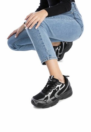 Zapatillas deportivas negras con detalles blancos, material de malla, diseño con cordones y suela texturizada, combinadas con jeans de color azul claro.