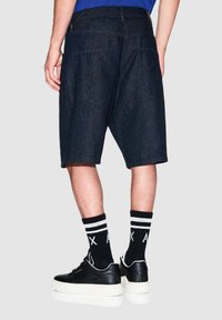 Shorts in denim blu scuro, dal taglio morbido, con tasche posteriori e orlo grezzo. Indossati con scarpe in pelle nera e calze a righe nere.