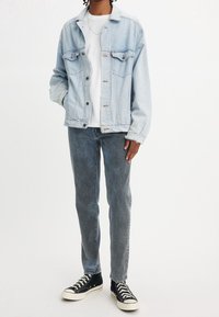 Ljusblå jeansjacka med två bröstfickor, vit t-shirt, grå jeans och svarta höga sneakers med vita sulor.