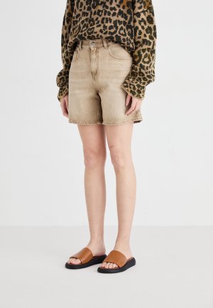 Shorts en denim beige avec un ourlet effiloché, portés avec un pull brun à motifs. Sandales à glissière brunes avec une semelle noire. Design minimaliste.