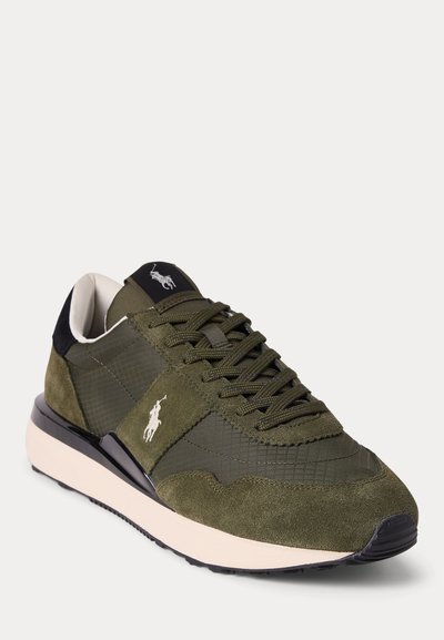 Alyvuogių žalios spalvos sportbačiai su zomšos ir tinklelio panelėmis, baltas logo šone, juodas kulno akcentas, smėlio spalvos vidurinė dalis ir juoda pado dalis, žiūrint kampu.