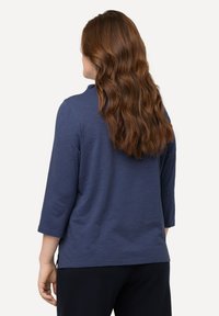 Navy blue, long-sleeve top with a round neckline and a relaxed fit. Made from soft fabric, featuring side slits at the hem.