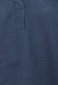 Gros plan sur un tissu en lin bleu foncé avec un tissage visible et une couture verticale près du centre supérieur.