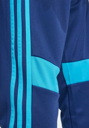 Gros plan sur un pantalon bleu marine avec trois bandes verticales bleu clair et un panneau horizontal bleu clair sur la cuisse.