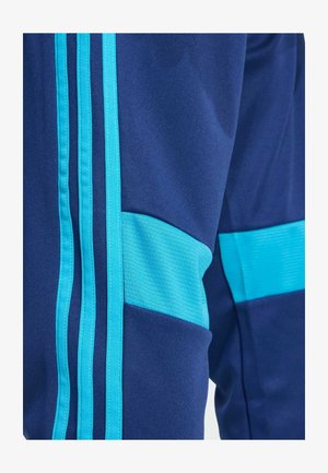 Close-up van donkerblauwe broek met drie verticale lichtblauwe strepen en een horizontaal lichtblauw paneel op de dij.