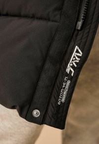 Čierna puffová bunda s prešívanou textúrou, ktorá má zips, značkovú nálepku a strieborný patent na šve.