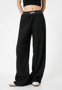 Zwarte wijde broek met een elastische tailleband, gemaakt van een gladde stof. Heeft een label op de tailleband en een comfortabele pasvorm.