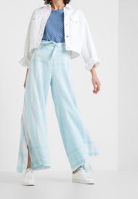 Giacca bianca corta, top blu a motivi, pantaloni larghi azzurri con motivi geometrici e sneakers bianche.