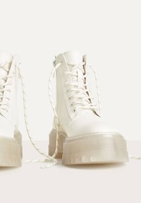 Vita snörning plattform stövlar med en kraftig, genomskinlig gummisula och texturerad ovandel, med randiga snören och sidodragkedjedetalj.