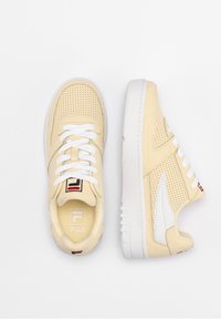 Paire de baskets FILA beiges perforées avec semelles et lacets blancs, affichée en vues de dessus et de côté sur fond blanc.
