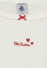 T-shirt bianco in cotone con ricamo rosso di "Petit Bateau" e due piccole cuori. Presenta un fiocchetto in satin rosso e un colletto scallop. Etichetta della taglia visibile.