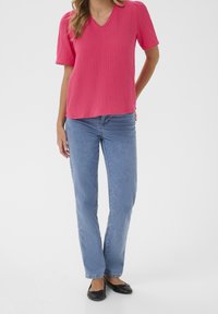 Rosa, strukturiertes Kurzarmoberteil mit V-Ausschnitt, kombiniert mit hellblauen, geraden Jeans und schwarzen Ballerinas. Einfaches Design, lässige Passform.