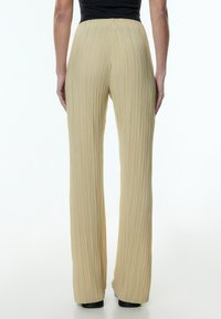 Gepliceerde, lichtbeige broek met een wijde pijpdesign, elastische tailleband en een gladde textuur, met verticale plooien van de taille tot de zoom.