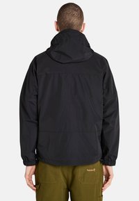 Musta huppari, jossa on elastiset hihansuut ja kiristettävä helma. Valmistettu kevyestä materiaalista, jossa on logo takana.