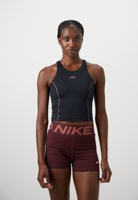 Čierny skrátený športový top s ružovými akcentmi a logom Nike, spárovaný s bordovými šortkami s výrazným opaskom Nike.