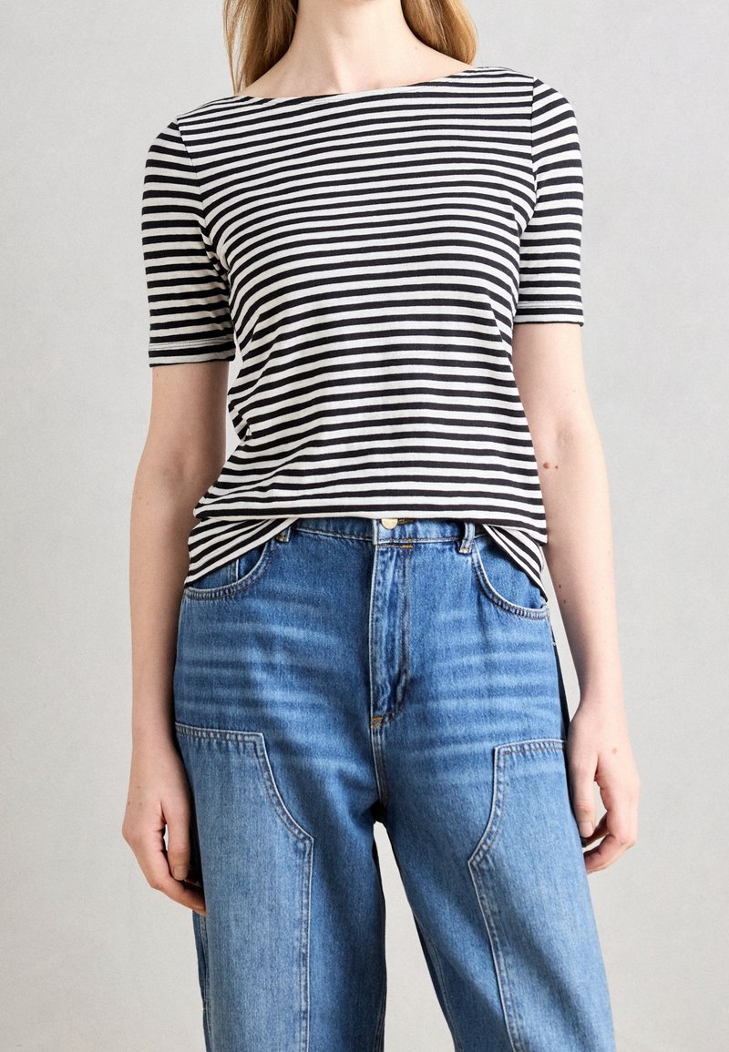 Camisa de manga corta a rayas blancas y negras con un escote amplio, combinada con pantalones vaqueros azul de talle alto con bolsillos parche y detalles desgastados.