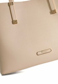 Beige gestructureerde tote bag gemaakt van textuurmateriaal, met gouden accenten en een merkimago. Glad design met een vlakke bodem.