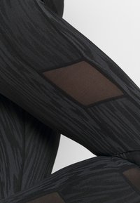 Czarne legginsy z teksturowanym wzorem o subtelnym połysku, przezroczystymi siateczkowymi panelami w kształcie diamentów oraz dopasowanym krojem.