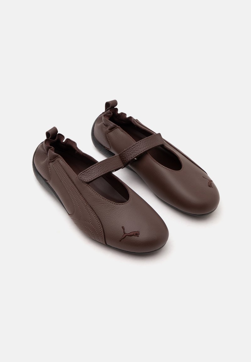 Chaussures style Mary Jane en cuir marron avec dos élastique, une bride sur le cou-de-pied et logo Puma sur les bouts arrondis.